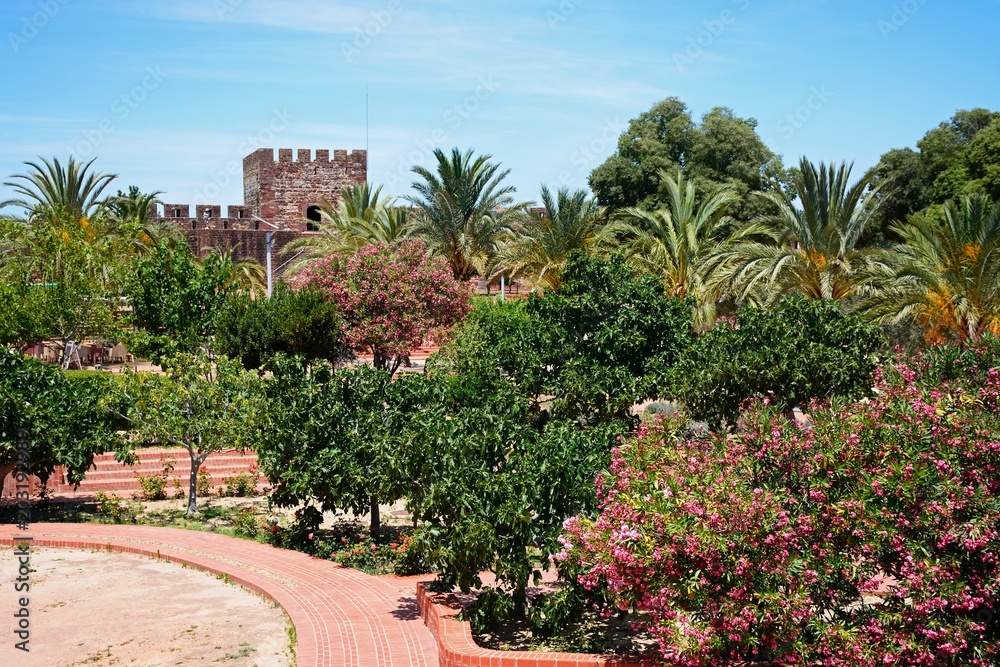 Courtyard gardens inside the Medieval castle with battlements and tower to the rear, Silves, Portugal.