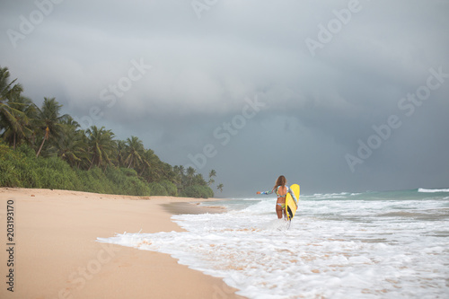 Girl surfer holds a board and goes into the ocean.