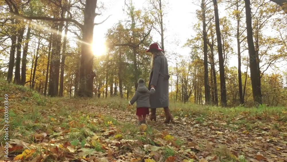 fashionable woman and daughter are walking in the autumn park on a sunny day fashionable woman and daughter are walking in the autumn park on a sunny day