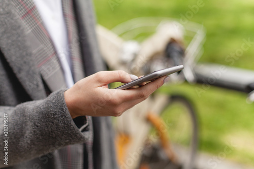 Close-up shot of hands using smartphone, young girl using bicycle rent mobile app smiling outdoors, cropped female manager browsing smartphone standing near bike sharing, healthy city lifestyle