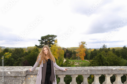 Cute girl standing near concrete railing with green trees background. Concept of architectural elements and visiting Europe. photo