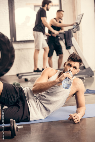 Fototapeta Naklejka Na Ścianę i Meble -  handsome sportsman drinking water from bottle in gym