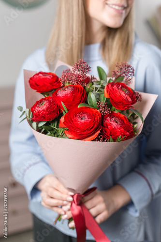 Sunny spring morning. Young happy woman holding a beautiful bunch of red buttercups or Ranunculus in her hands. Present for a smiles girl. Flowers bouquet