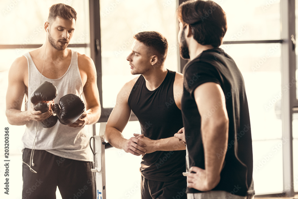 three athletic young men on sportswear talking in gym