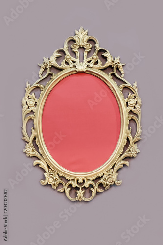 Openwork oval golden colored frame on wall at grey background.