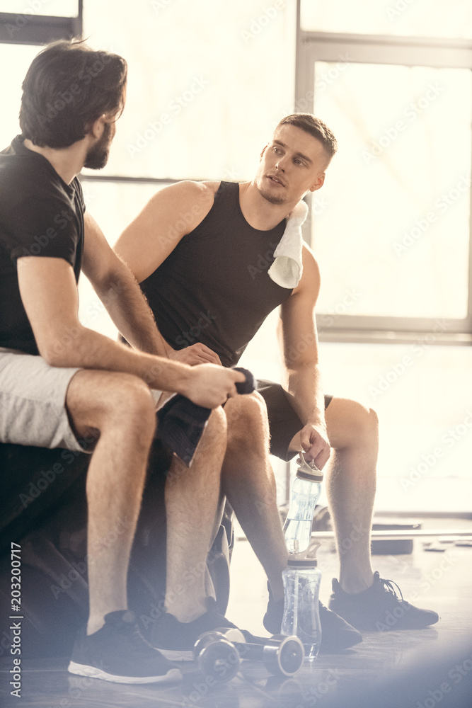 Obraz premium two young sportsmen sitting on tire and looking at each other after workout in gym