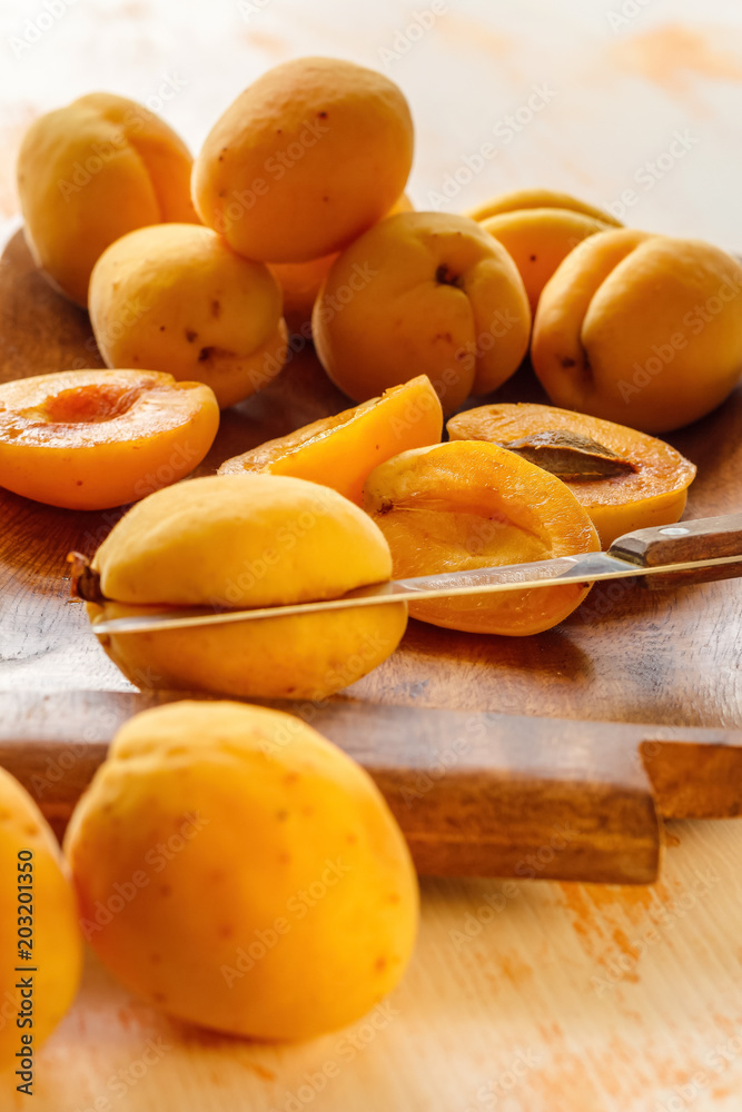 The process of manual cleaning of apricots from bones using a kitchen knife on a wooden dish. Preparation for cooking jam. Lifestyle
