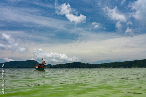 Green Longtail boat moored in Saracen Bay in Koh Ron Samloem, Cambodia. Beautiful clouds on the sky in the background. 