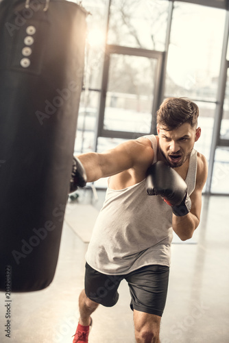 emotional young sportsman training with punching bag in gym
