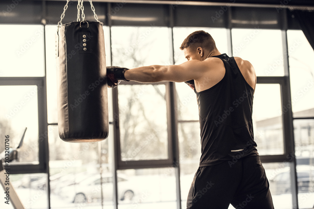 side view of muscular young boxer training with punching bag in gym