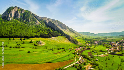 Aerial view of Rimetea, Transylvania, Romania. Grass meadow with wild flowers and the limestone rock Piatra Secuiului dominating the countryside. Drone shot