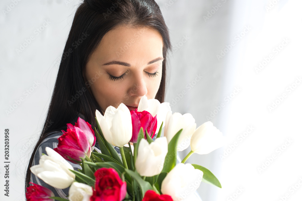 portrait of beautiful woman with eyes closed and bouquet of tulips at home