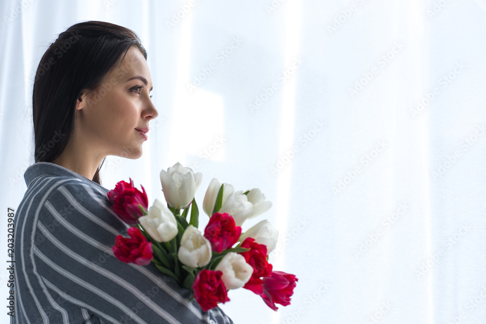 side view of beautiful pensive woman with bouquet of tulips at home side view of beautiful pensive woman with bouquet of tulips at home