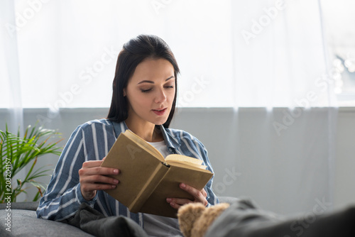 portrait of young woman reading book on sofa at home