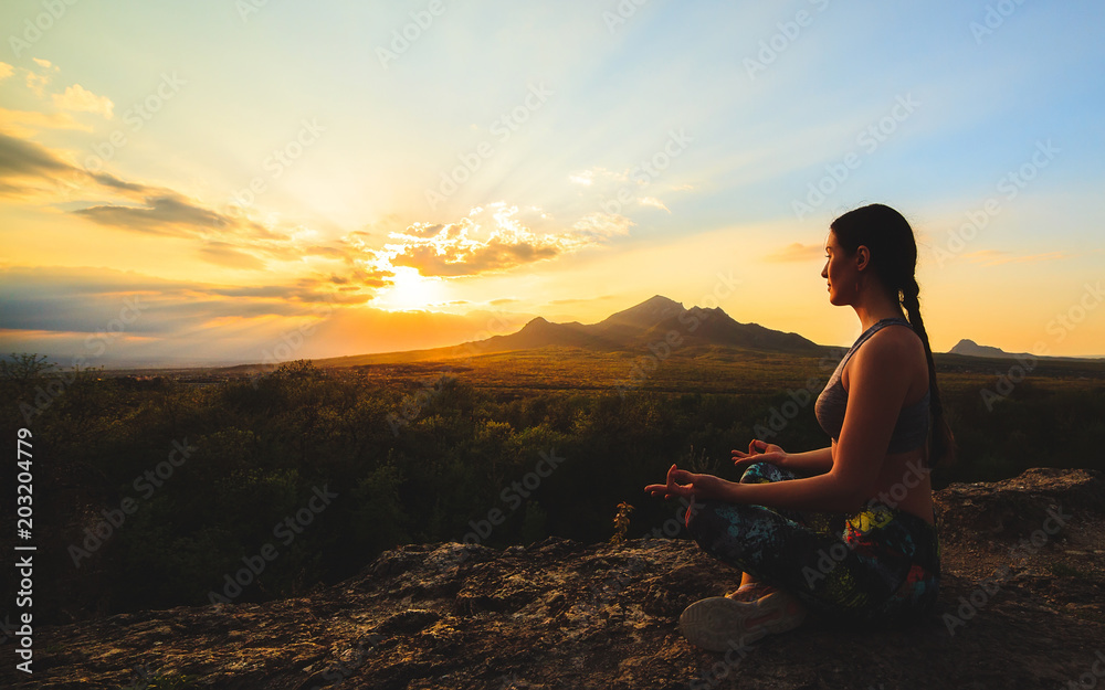 Young woman practicing yoga or pilates at sunset or sunrise in beautiful mountain location.