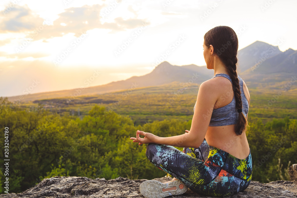 Young woman practicing yoga or pilates at sunset or sunrise in beautiful mountain location. Young woman practicing yoga or pilates at sunset or sunrise in beautiful mountain location.