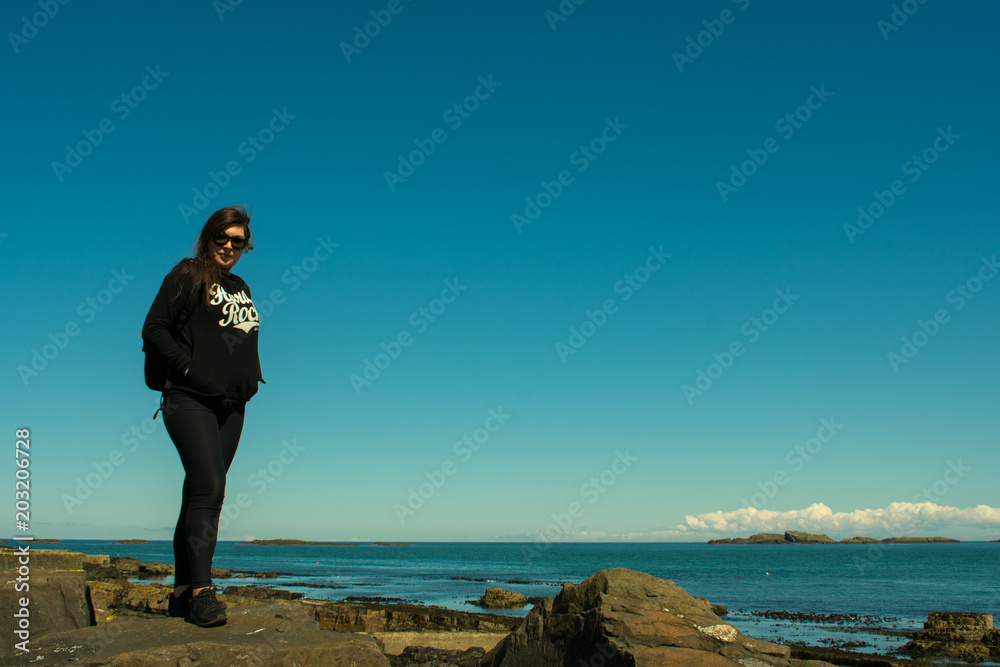 beautiful woman with dark hair dressed black standing on rock formations and looking on ocean. beautiful woman with dark hair dressed black standing on rock formations and looking on ocean.