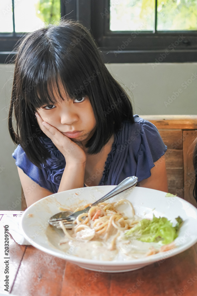 Unhappy Asian girl kid getting bored of food with appetite loss, no hungry habit, eating disorder Unhappy Asian girl kid getting bored of food with appetite loss, no hungry habit, eating disorder