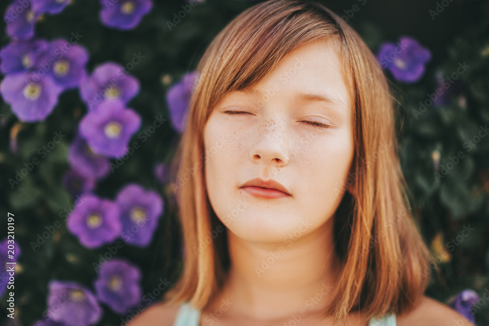 Daydreaming pretty kid girl, close up portrait against purple flower wall. Eyes closed