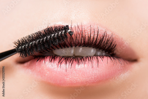 cropped image of woman applying mascara on eyelashes in mouth isolated on white