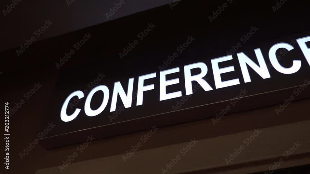 LED information sign ≪Conference Hall≫ above the door in dim light, close-up. A bright white light sign above the door in a dark business center hall. LED information sign ≪Conference Hall≫ above the door in dim light, close-up. A bright white light sign above the door in a dark business center hall.