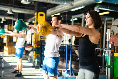 Close up front view of focused and motivated strong young fitness couple in sportswear doing exercizes crouching with the kettlebells reversed and doing squats in the gym at sunny day