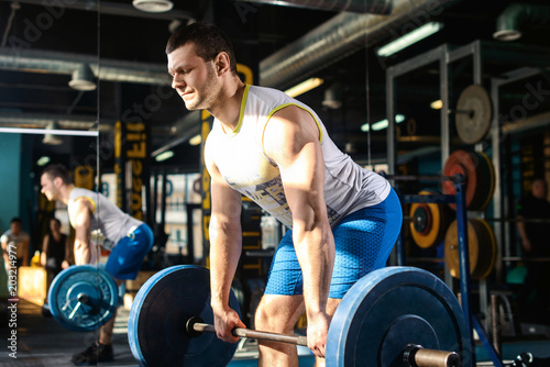 European caucasian athletic man doing deadlift with heavy barbell. man lifting barbell opposite window. Moment of lifting weight. Healhy lifestyle, fitness, crossfit and bodybuilding