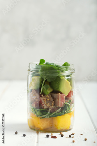 Hawaiian Poke salad with tuna, avocado, mango and vegetables in a jar on a white wooden rustic background