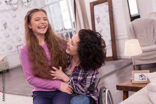 Time together. Exuberant disabled woman laughing with girl who sitting on her knees