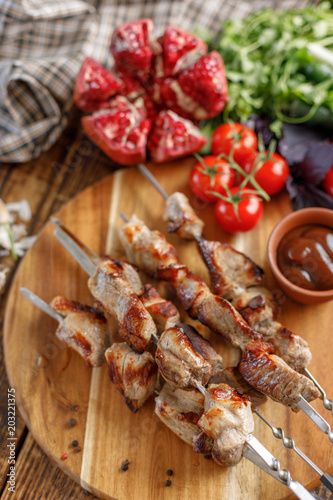 Shish kebab from pork on a wooden background. Appetizing meat cooked on an open fire and fresh vegetables. Rustic.
