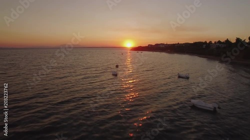 Flying over the sea and moored boats near the coast with resort town, scene at sunset. Trikorfo Beach, Greece photo