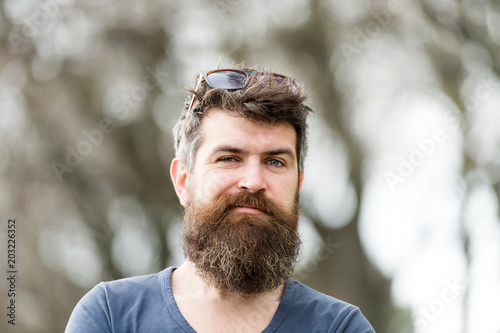 Man with long beard and mustache wears sunglasses on head, defocused background. Hipster with beard with gray on cheerful face. Barbershop concept. Guy looks cool with stylish beard and haircut.