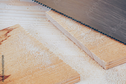 A saw and a sawn off plank with a background of pine wood with sawdust on. Concept for being a handyman, craftsman and renovate house.