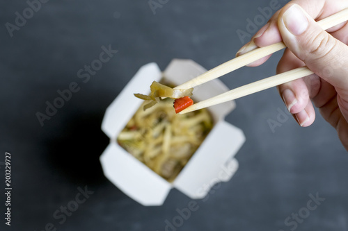 Hand holding chopsticks with vegetables on the background of an open box with food