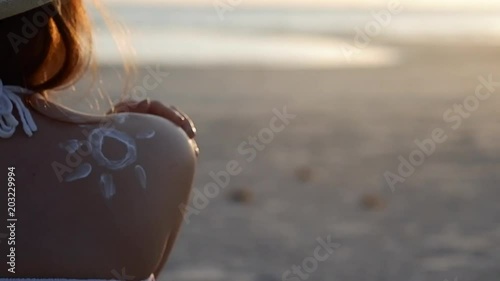 Close up beautiful young woman applying sun protection cream to shoulder on tropical sea beach in summer. Female beauty and skin care use sunscreen, sunblock, to protect skin for sunburn.