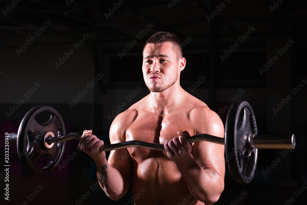 Muscular young man lifting weights on dark background Muscular young man lifting weights on dark background
