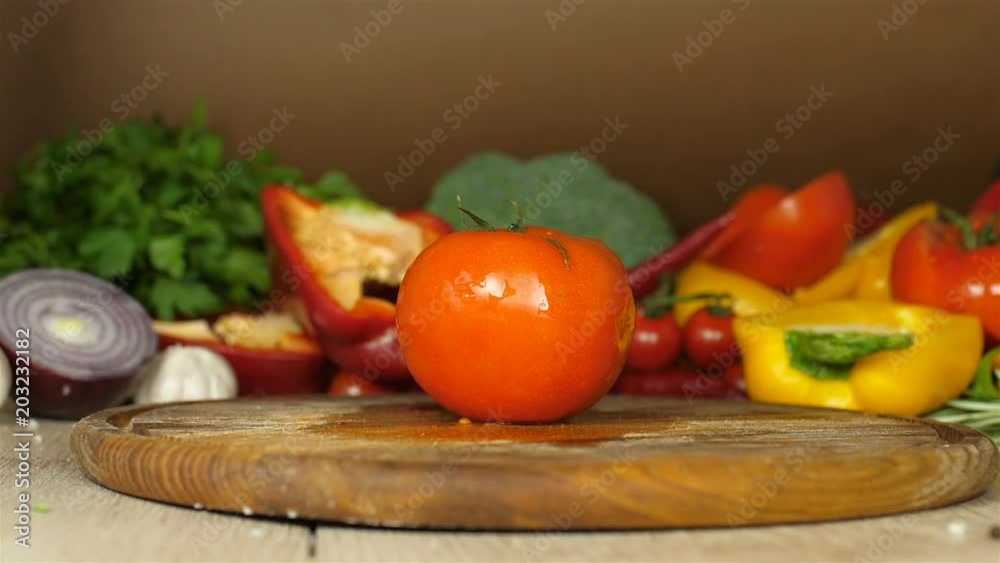Chef in black gloves lays juicy red tomato with dripping water droplets close-up lies on a wooden board on a background of green, red pepper, brocoli, background blur, video close up, restaurant Chef in black gloves lays juicy red tomato with dripping water droplets close-up lies on a wooden board on a background of green, red pepper, brocoli, background blur, video close up, restaurant