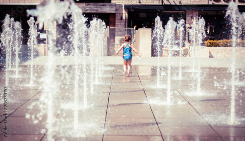 Cute Little Girl in Blue Swimming Suit Playing with Water jets of Street Fountain, Hot Summer Day, Kids Fun, in England, Dorchester