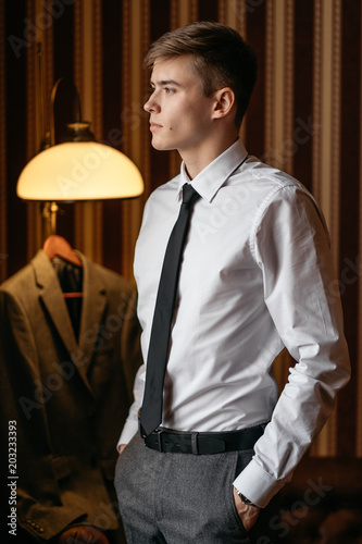 A young handsome man in a business suit is standing in a room with striped wallpaper