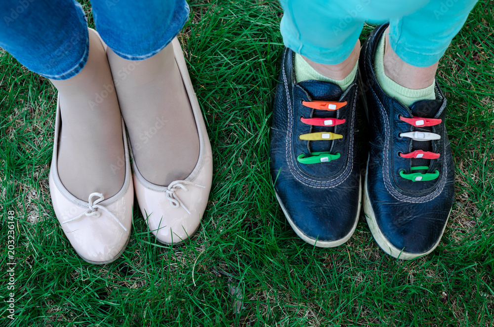 Two people are standing on green grass near each other shod in ballet flats and sneakers.