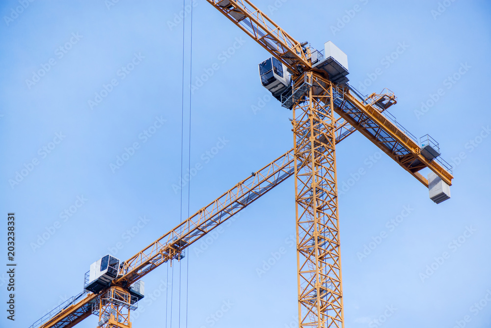 Close up of crane doing construction work on block building. New buildings being constructed. Industrial building site. Shot of lifting crane and skyscraper under construction on clear blue sky