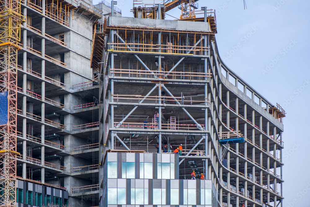 New residential and office block buildings being constructed. Industrial building site. Workers putting windows in under construction skyscraper
