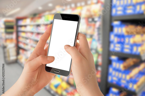 Female hands holding smartphone with empty screen, blurred grocery store in background. Online shopping concept, Mockup