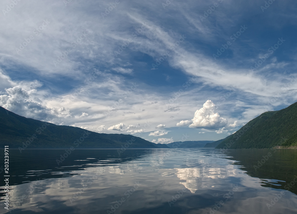 panorama of a mountain lake with reflection of the sky and white clouds in calm water