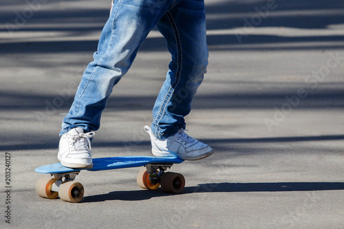 Little the boy in light blue jeans learning to roller skate in summer park. Active outdoor sport for kids. Close up view of legs on skate