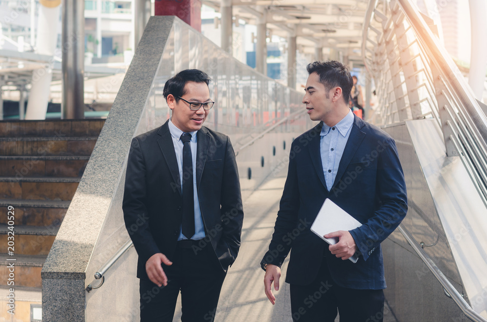 two attractive business man discussion holding tablet and walking at outdoor walk way in city on morning.