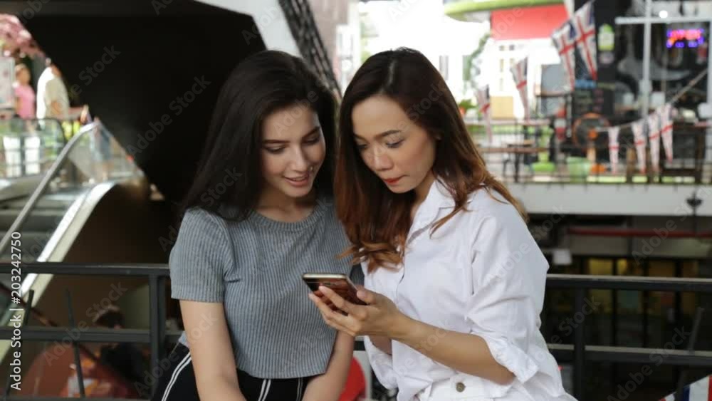 Asia girl and friend ethnic German-Thai taking smart phone selfie in department store.
