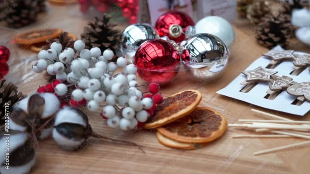Pine cones, artificial berries, christmas tree balls, cotton ball flowers and dry orange slices on plastic wrap, close-up. Supply for handcrafted decorations on wooden table. Christmas atmosphere. Pine cones, artificial berries, christmas tree balls, cotton ball flowers and dry orange slices on plastic wrap, close-up. Supply for handcrafted decorations on wooden table. Christmas atmosphere.