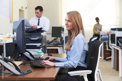 Businesswoman Working At Computer In Busy Office