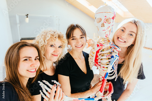 Selfie portrait of four happy smilling team female pilates instructor hugging with skeleton model in modern pilates studio interior. Sport, fitness, lifestyle, gesture and team work concept. photo
